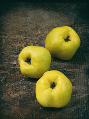 Three ripe yellow quince on a wooden background