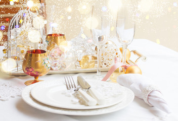 Tableware for christmas - set of plates, cups and utencils with white table cloth and christmas golden decorations with bokeh lights