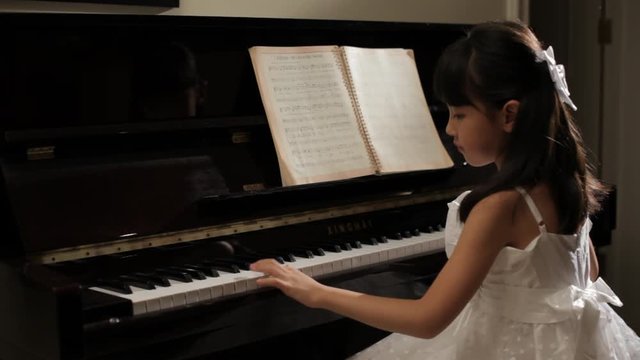 MS Rear view of girl wearing white dress, playing piano / China