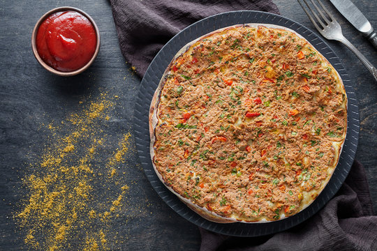 Lahmacun traditional turkish delicious pizza with minced beef or lamb meat, paprika, tomatoes, cumin spice, parsley baked spicy middle eastern arabian food on dark table background