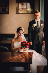 luxury wedding couple holding hands and sitting in cafe in morning near window in soft light. elegant gorgeous bride and stylish groom in retro style. romantic moment