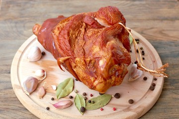 Smoked pork meat knuckle with garlic, pepper and laurel bay on wooden background