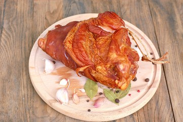 Smoked pork meat knuckle with garlic, pepper and laurel bay on wooden background