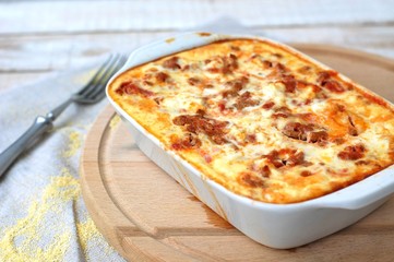 Gluten free meal roasted polenta with pork meat, spring onion, spices in white pan on grey cloth on white wooden background