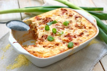 Gluten free meal roasted polenta with pork meat, spring onion, spices in white pan on grey cloth on white wooden background