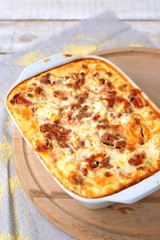 Gluten free meal roasted polenta with pork meat, spring onion, spices in white pan on grey cloth on white wooden background