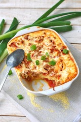 Gluten free meal roasted polenta with pork meat, spring onion, spices in white pan on grey cloth on white wooden background