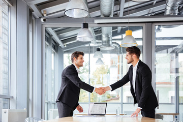 Two happy businessmen standing and shaking hands on business meeting