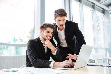 Fototapeta premium Two cheerful young businessmen using laptop on business meeting together