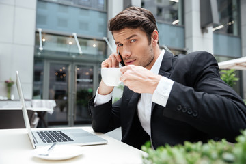 Businessman with laptop talking on mobile phone and drinking coffee