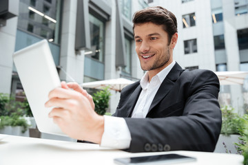 Happy young businessman using tablet in outdoor cafe