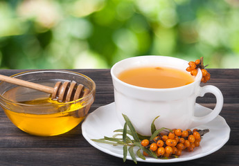 Tea of sea-buckthorn berries with honey on wooden table  blurred garden background