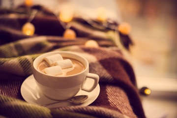 cup of coffee with marshmallows, warm blanket and Christmas ligh