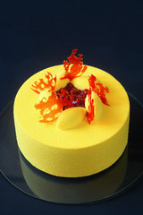 Contemporary Yellow Velvet Mousse Cake decorated with red caramel and wild strawberries, on dark blue background.