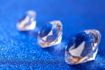 Three grand expensive diamonds laid on the diagonal on blue sparkling sequins background, macro . Big brilliant closeup.