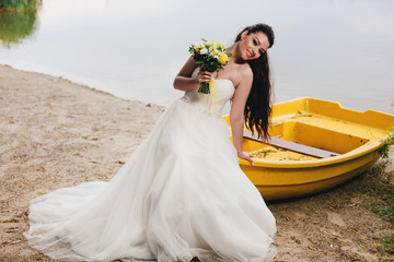 Bride sitting on the boat on the river bank