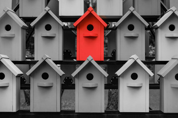 Red color wooden birdhouse stand out from the crowd. Metaphor to business concept. Stands out among...