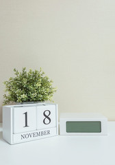 White wooden calendar with black 18 november word with clock and plant on white wood desk and cream wallpaper textured background , selective focus at the calendar