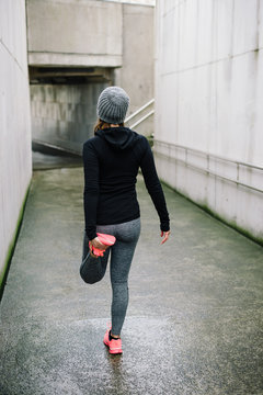 Sporty woman stretching quadriceps and warming up for running urban fitness winter workout. Sport and healthy lifestyle concept. Female runner exercising outside.