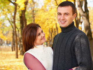 Fototapeta premium happy adult couple embrace in autumn city park, trees with yellow leaves, bright sun and happy emotions, tenderness and feelings