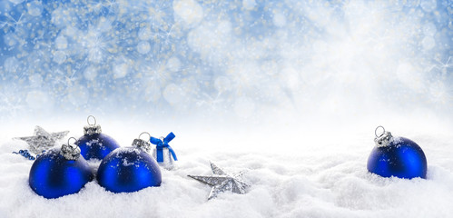 Blaue Weihnachtskugeln, ein Glöckchen und Sterne im Schnee vor sonnigem Bokehhimmel, Panorama