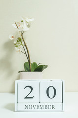 Closeup white wooden calendar with black 20 november word with white orchid flower on white wood desk and cream color wallpaper in room textured background , selective focus at the calendar