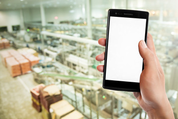 Hand holding smart phone on Manufacturing factory blurred background.