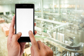 Hand holding smart phone on Manufacturing factory blurred background.
