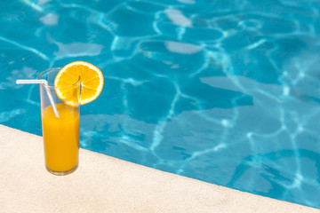Glass of orange juice in the edge of swimming pool