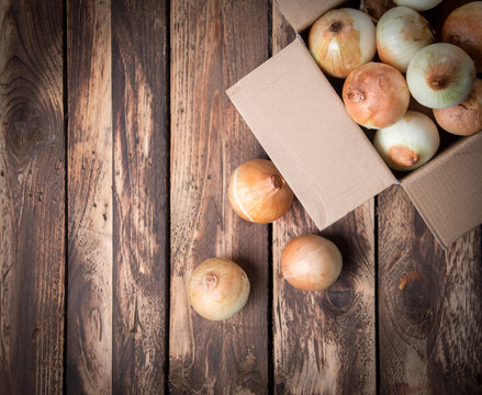 Raw onions in paper box on wooden table