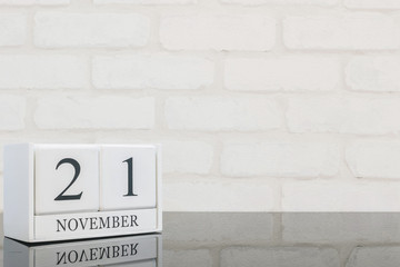 Closeup white wooden calendar with black 21 november word on black glass table and white brick wall textured background with copy space , selective focus at the calendar