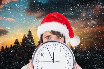 Woman in santa hat holding a wall clock against digitally genera