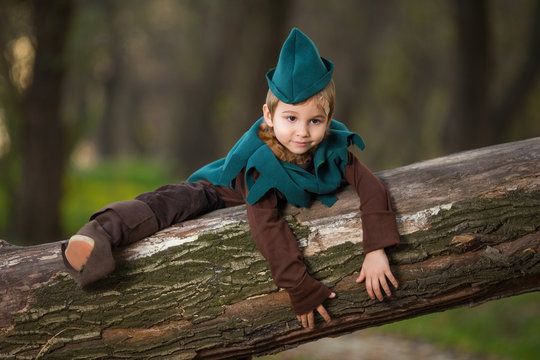 Little boy is playing in forest. He is dressed up as a knight and he is lying down on a tree branch