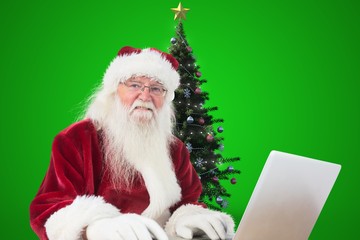 Naklejka premium Santa claus using laptop against green background