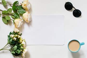 White desk with coffee cup, sunglasses, roses and film camera. Empty sheet in the middle. Top view, flat lay, copyspace.