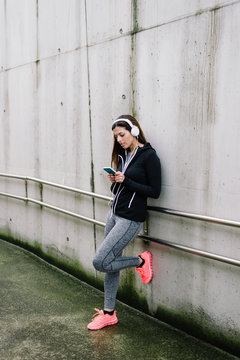 Sporty woman taking a workout rest for listening music and texting on smartphone. Female urban runner on winter training.