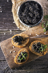 Black Astrakhan Russian salted sturgeon caviar in a can on dark background with wooden spoon and...