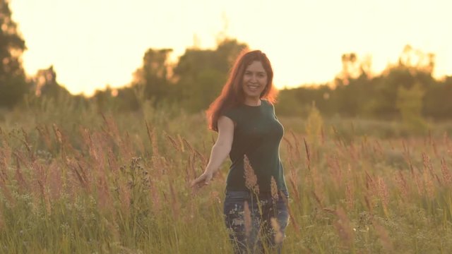 Cheerful young woman to whirl on the spot in the field at sunset.