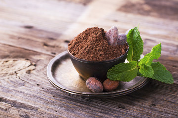 Cocoa powder and beans dry ripe  vintage metal German silver dish with a sprig of fresh fragrant mint on  simple wooden background. selective focus