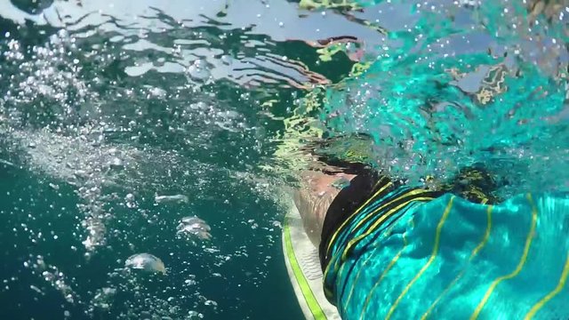SLOW MOTION OVER-UNDER: Unrecognizable person paddling out on surfboard in ocean