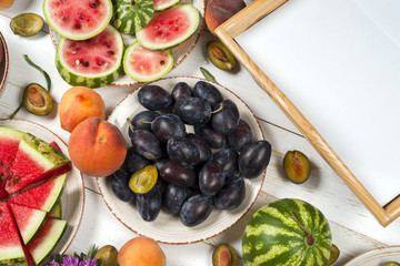 Colorful fruit set of purple, red and orange background in bowls. Plum, peaches, watermelon sliced above white tabletop