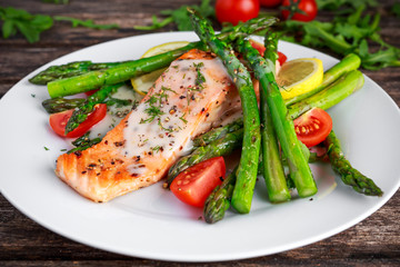 Fried salmon with asparagus, tomatoes, lemon, yellow lime on white plate