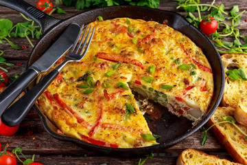 Frittata made of eggs, potato, bacon, paprika, parsley, green peas, onion, cheese in iron pan. on...