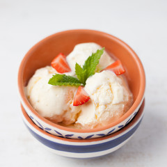 Dairy ice cream topped with mint and strawberries in the bowl on a  white table, selective focus