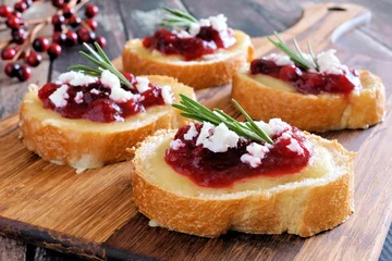 Tuinposter Holiday crostini appetizers with cranberry sauce, brie, feta and rosemary on a wooden server © Jenifoto