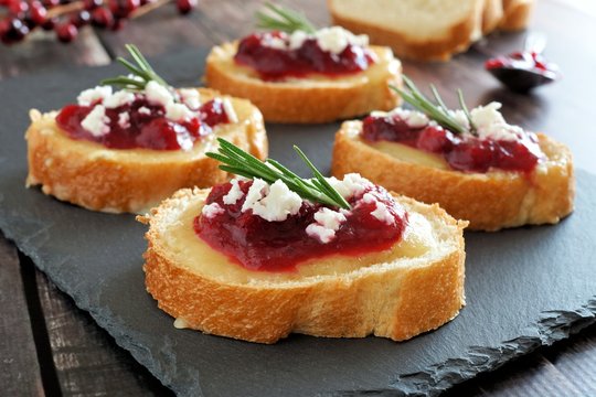 Holiday crostini appetizers with cranberry sauce, brie, feta and rosemary on a slate server
