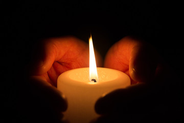 Hände halten und umfassen eine brennende Kerze in der Dunkelheit