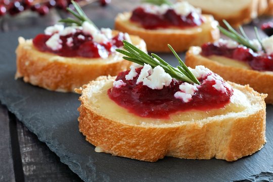Holiday crostini appetizers with cranberry sauce, brie, feta and rosemary close up on a slate server