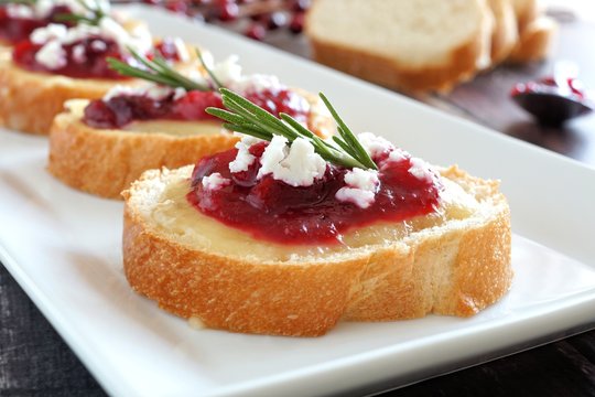 Holiday crostini appetizers with cranberry sauce, brie, feta and rosemary close up on a white plate