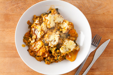 Overhead view of a lentil and vegetable hotpot with a cheesy potato topping in a white china bowl